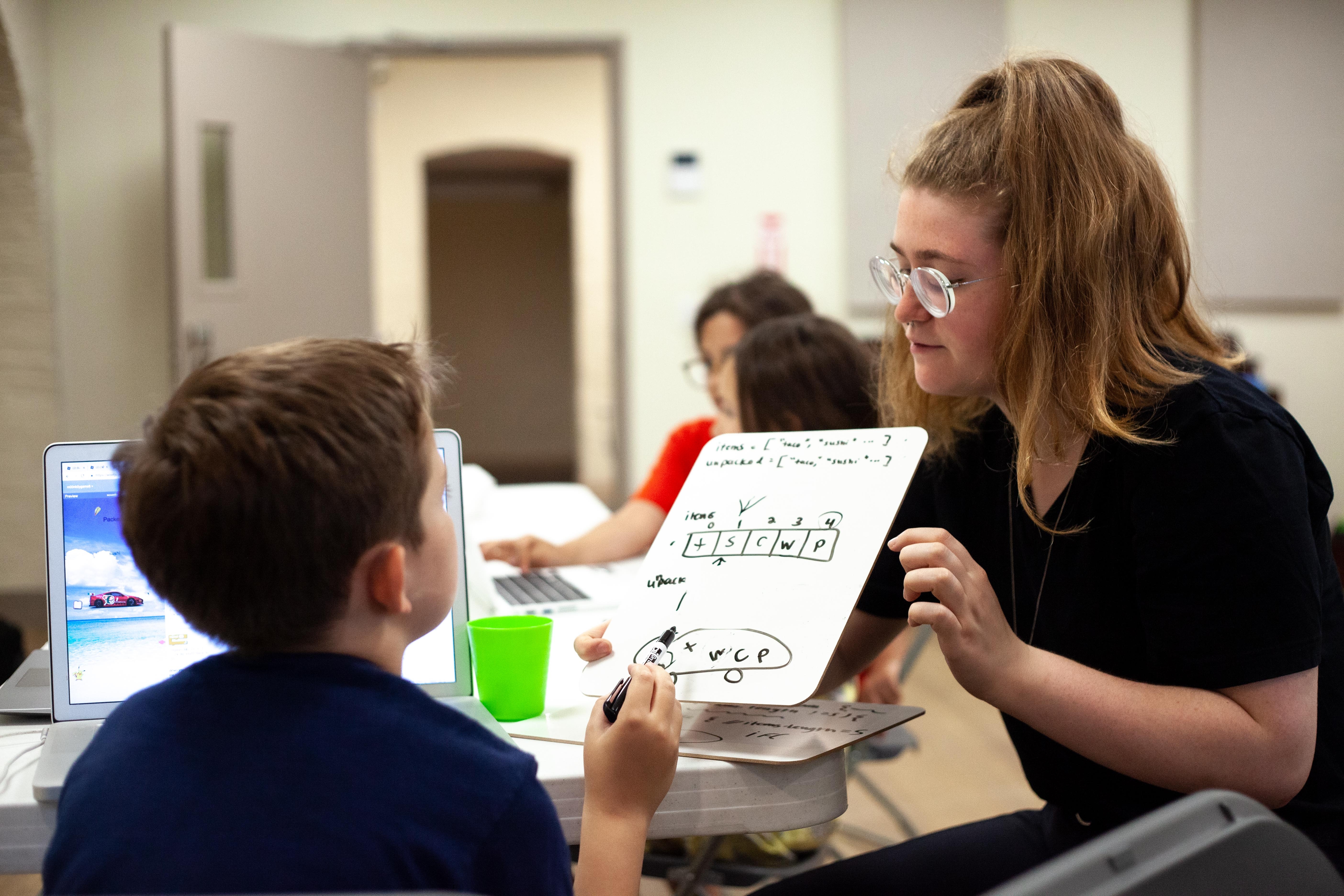 Instructor reviewing coding example on a white board in front of a kid.