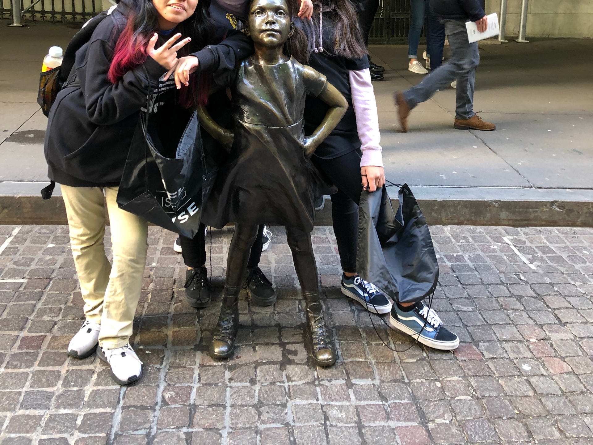 Group of students posing with statue of girl standing up to wall street
