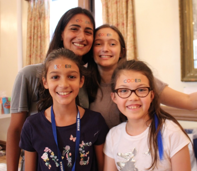 Girl coders with multicolor "coder" letters on their foreheads.