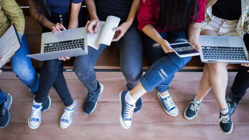 Group of faceless teens on computers, tables, notebooks.