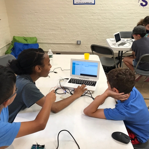 An instructor and two students gather around a computer with electronics hooked up to study circuits.